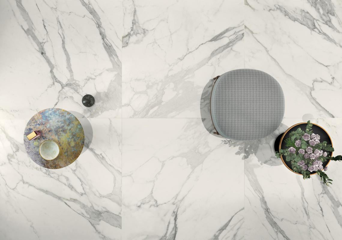 Three decorative items on a marble look tile surface: a round metallic object, a gray textured sphere, and a circular plant pot with flowers.