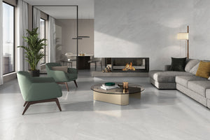 A modern living room with light gray stone-look porcelain floor tiles, featuring a gray sectional sofa, two green accent chairs, a round coffee table, and a built-in fireplace against a textured gray wall.