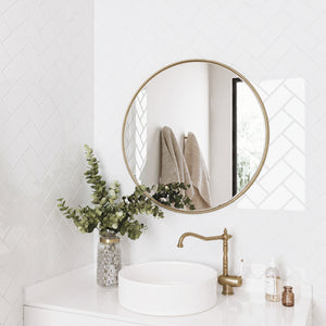 Bathroom with round gold mirror, white subway tiles, white sink, and greenery.