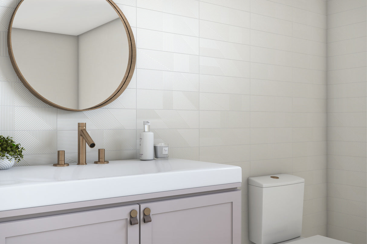 A modern bathroom vanity setup with a white countertop, matte brass faucet and cabinet hardware, a round wall mirror, white subway tile walls, and a white toilet visible in the background.