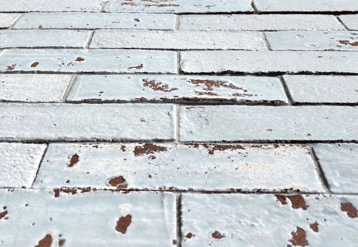 Low-angle view of Artesano Cozumel Blue 2x9 glossy clay brick tile showing crackled glaze and chipped edges