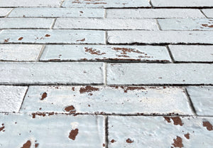 Low-angle view of Artesano Cozumel Blue 2x9 glossy clay brick tile showing crackled glaze and chipped edges