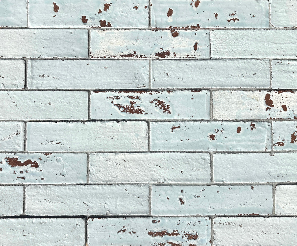 Artesano Cozumel Blue Glossy Brick 2x9 clay tile in a running-bond layout, pale blue crackle glaze with chipped red clay edges